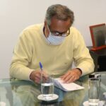 Presidente do CRMV-SP está de suéter bege, máscara e óculos, sentado à mesa assinando o protocolo de intenção.