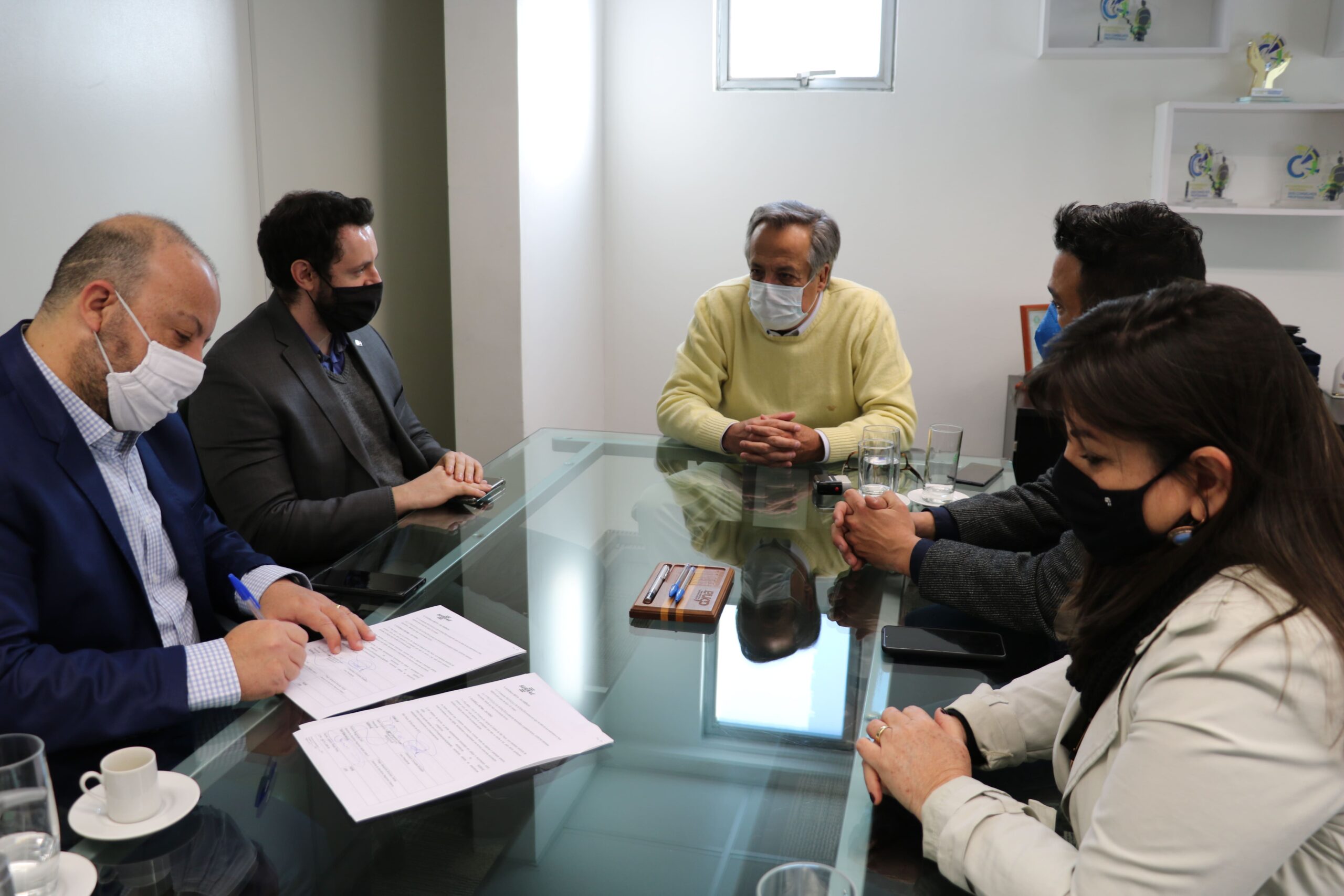 Consultor do Sebrae-SP assina protocolo de intenções, sendo observado pelos demais que estão sentados à mesa.