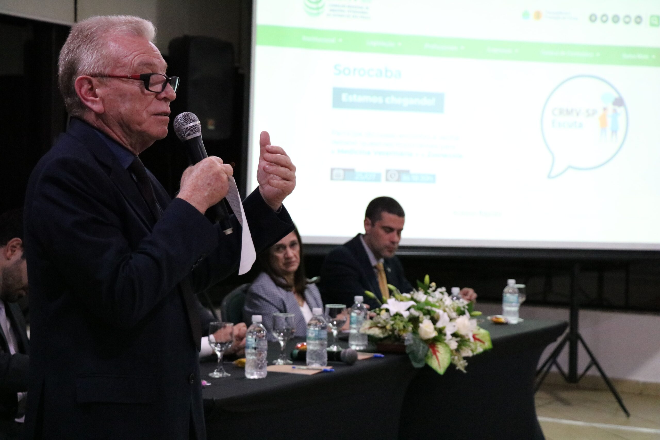 Na foto há o Presidente do CRMV-SP, Odemilson Donizete Mossero, em pé, vestindo terno e gravata segurando um microfone