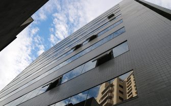 A imagem mostra a vista lateral nova do prédio, com janelas espelhadas e superfície em pastilha de cor verde.